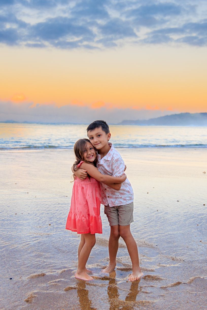 Two young children play together at the beach during a beautiful sunset.