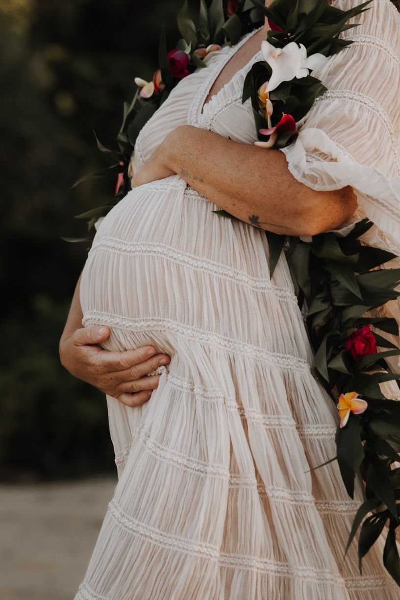 Close-up details of a white ruched maternity dress with delicate floral decorations.