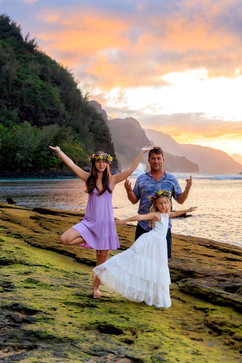 Dramatic sunset over Hawaiian coastline with moss-covered rocks and crashing waves.