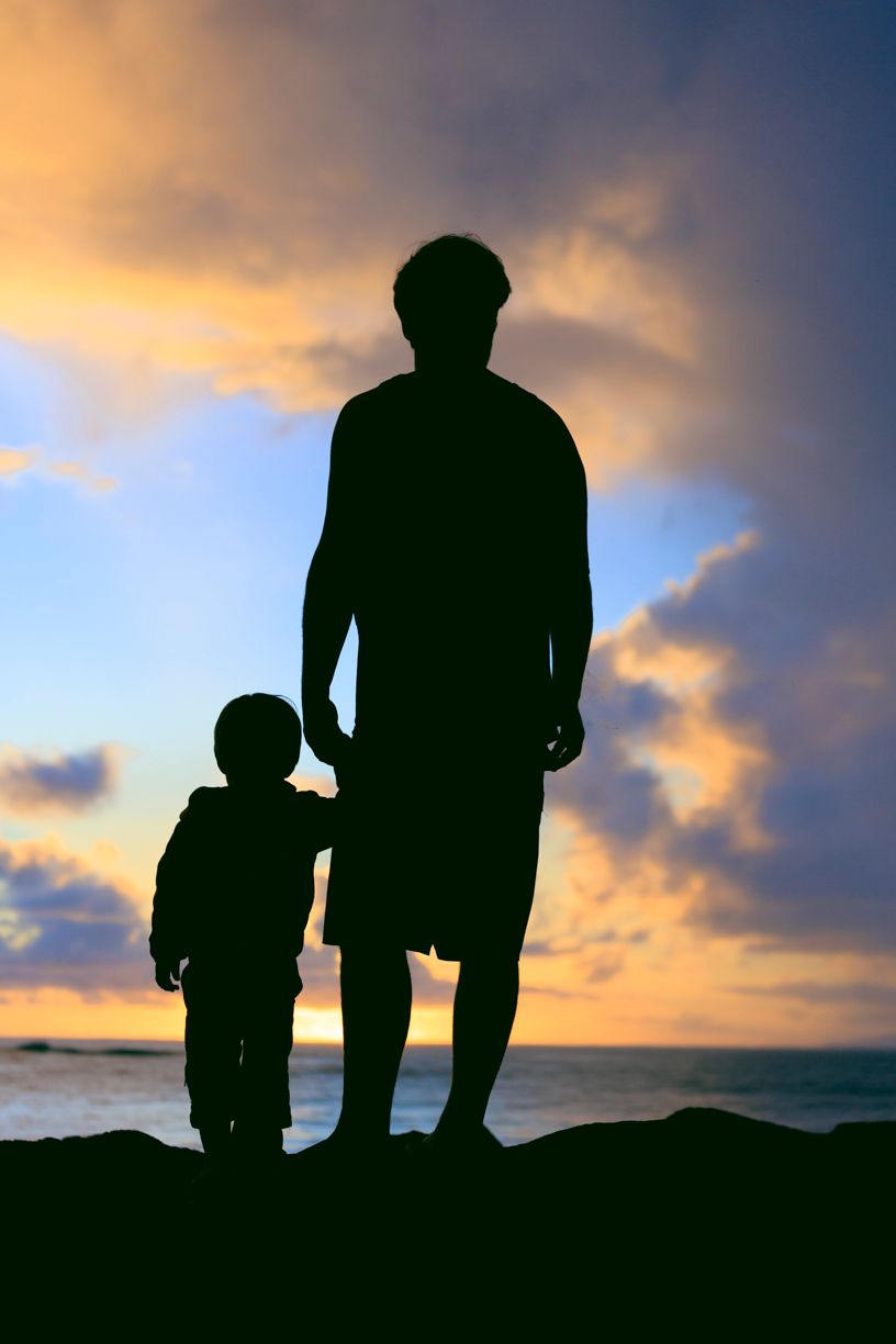 Silhouettes against a dramatic sunset sky on a Kaua'i beach shoreline.
