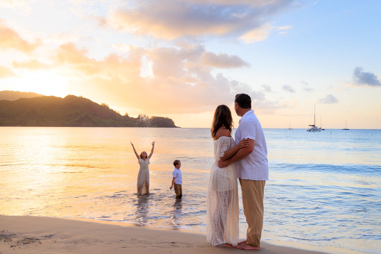 Family enjoying a sunset beach moment with mountains and sailboat in the distance at Hanalei Bay