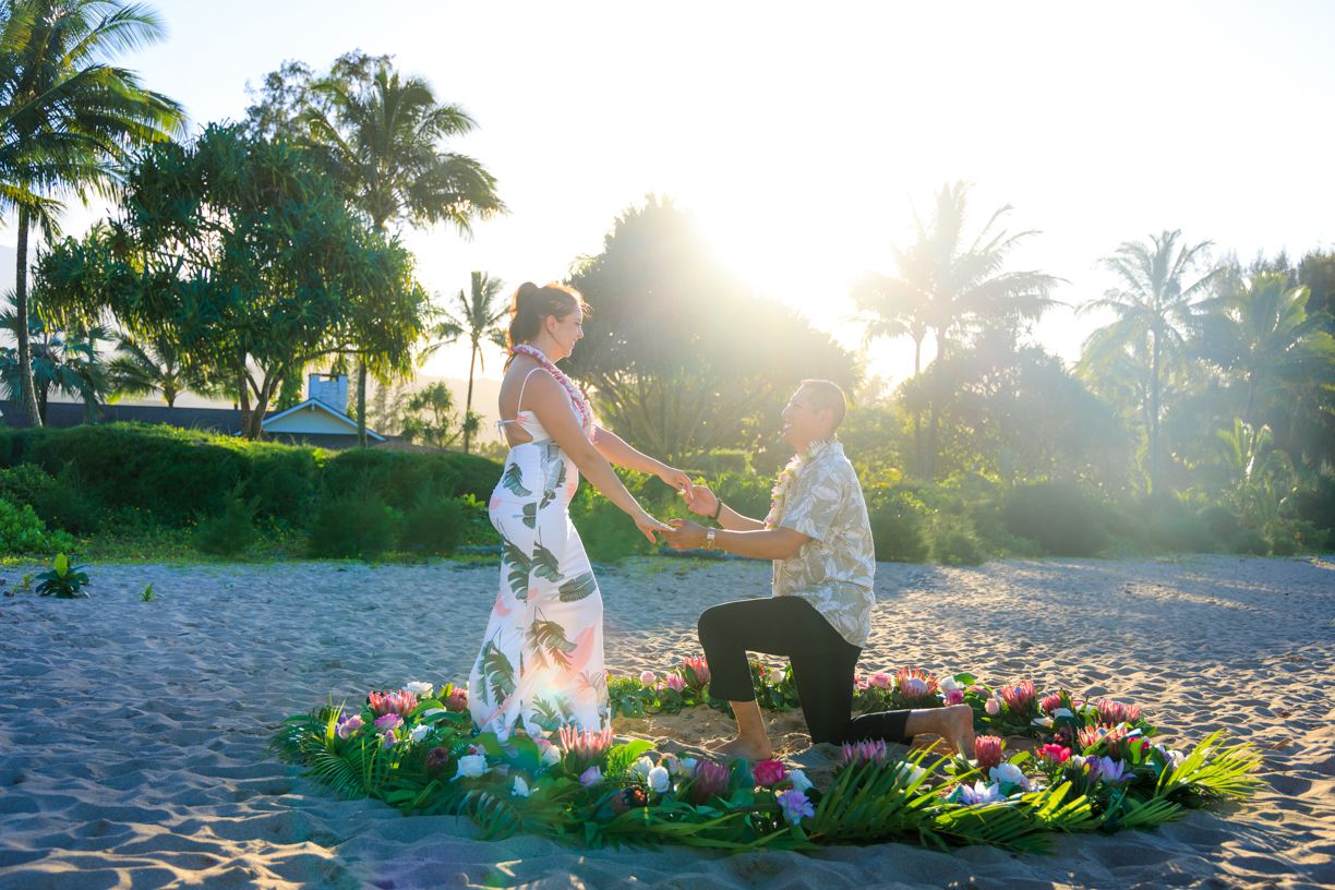 A couple enjoys a romantic photoshoot on a Hawaiian beach with tropical flowers and palm trees.