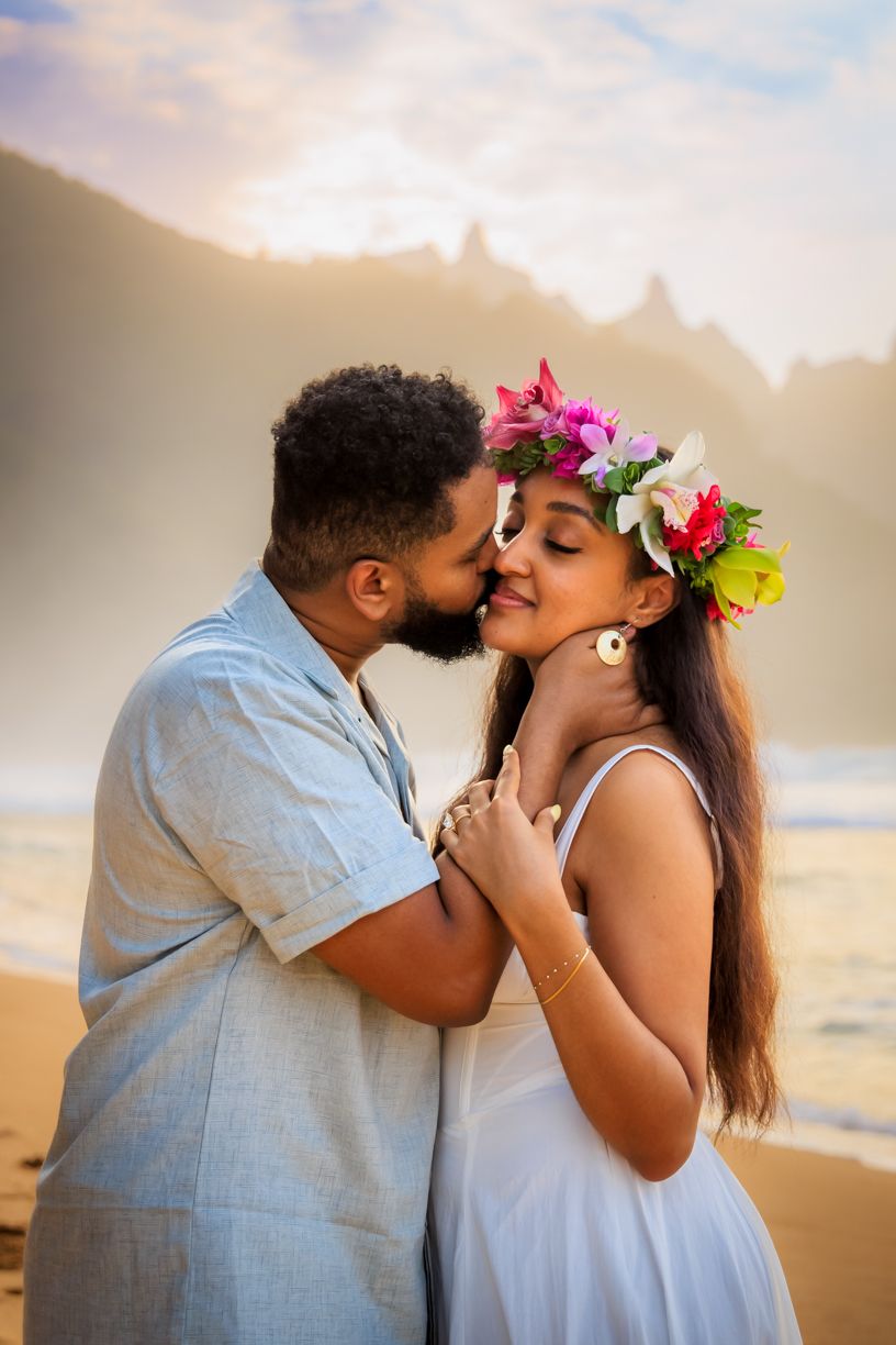 Couple in white sharing romantic moments on a beach at sunset.