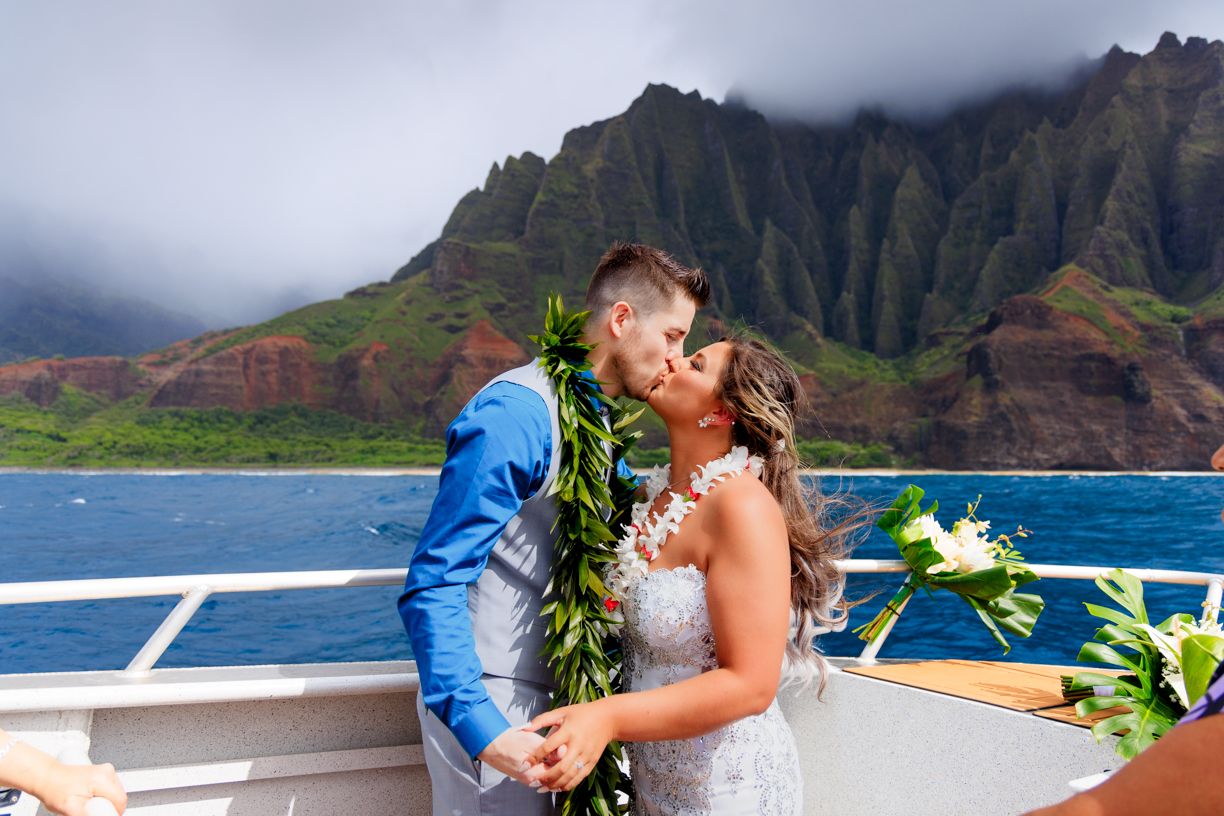 Wedding photo session on a boat with dramatic Hawaiian coastal cliffs in background.