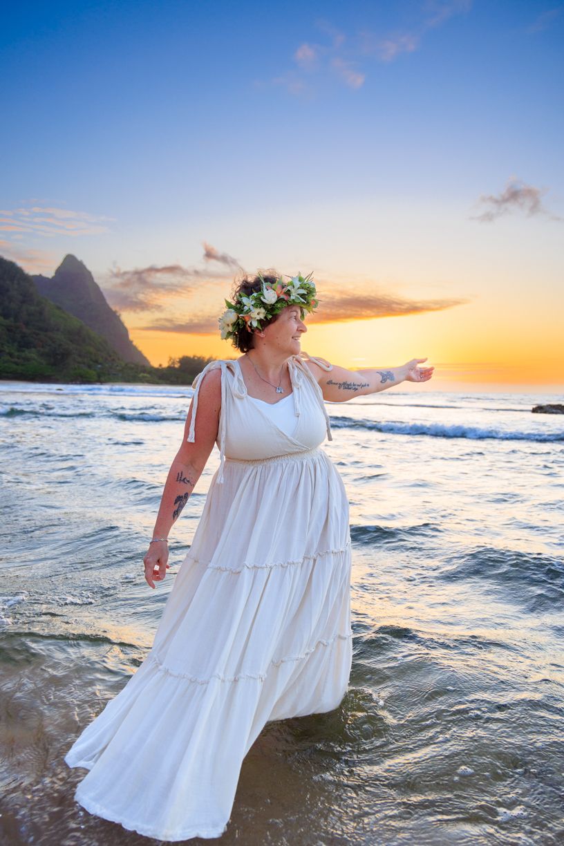 A flowing white dress billows in the ocean breeze at sunset with dramatic mountains and waves in the background.