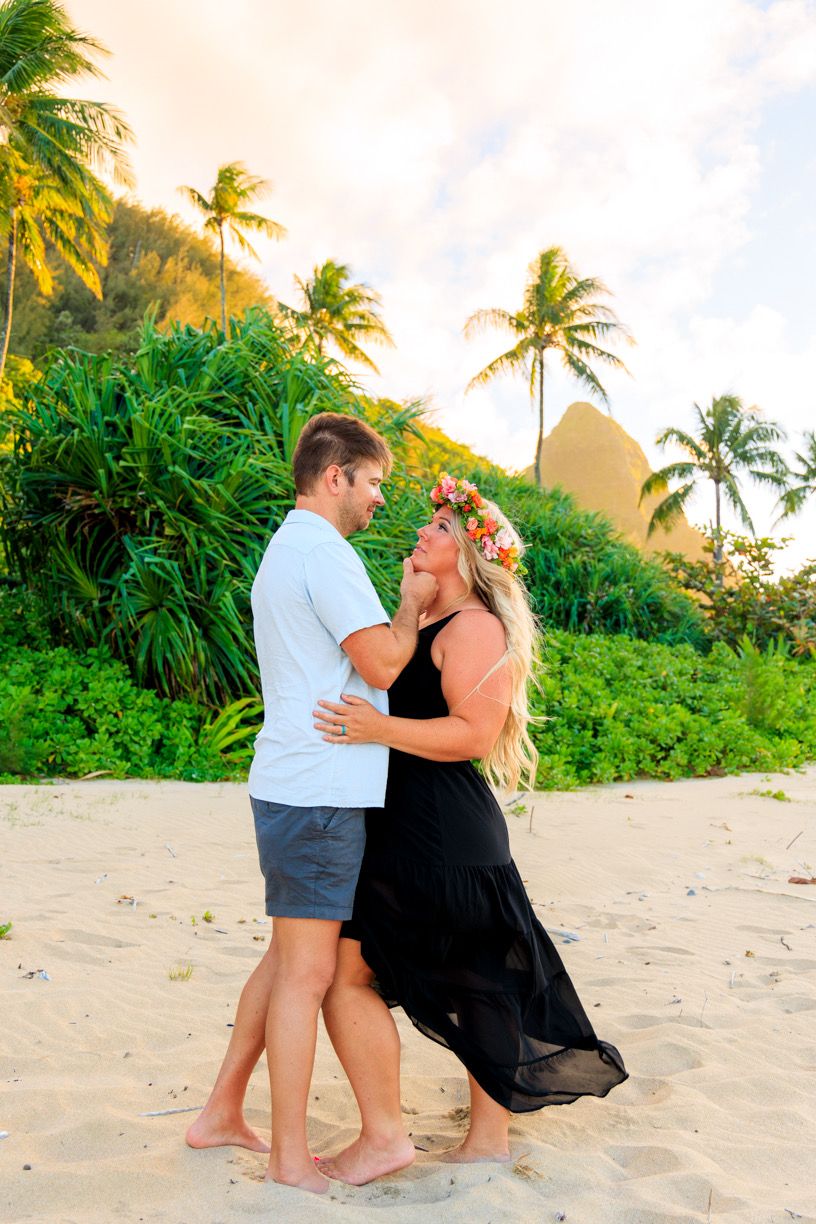 A romantic beach scene with a couple posing together against a backdrop of palm trees and mountains.