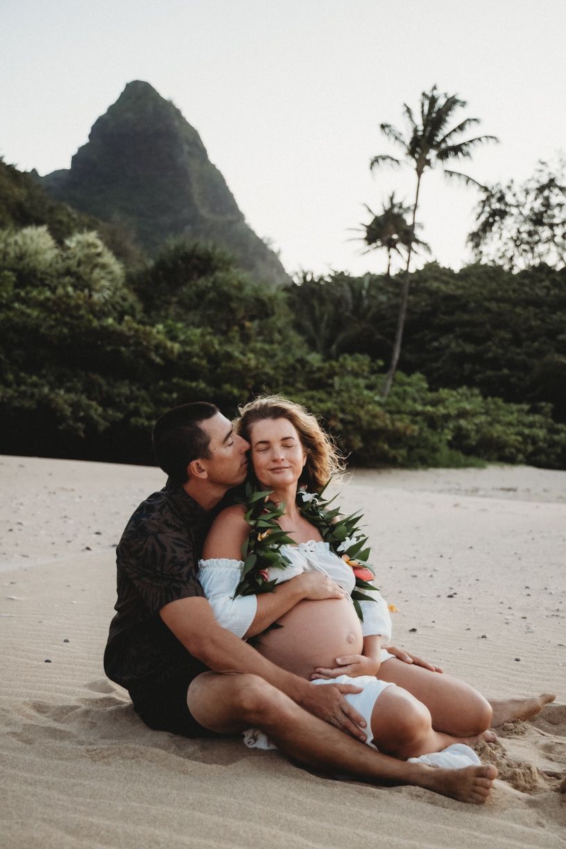Romantic beach maternity photos with dramatic mountain landscapes in Hawaii.