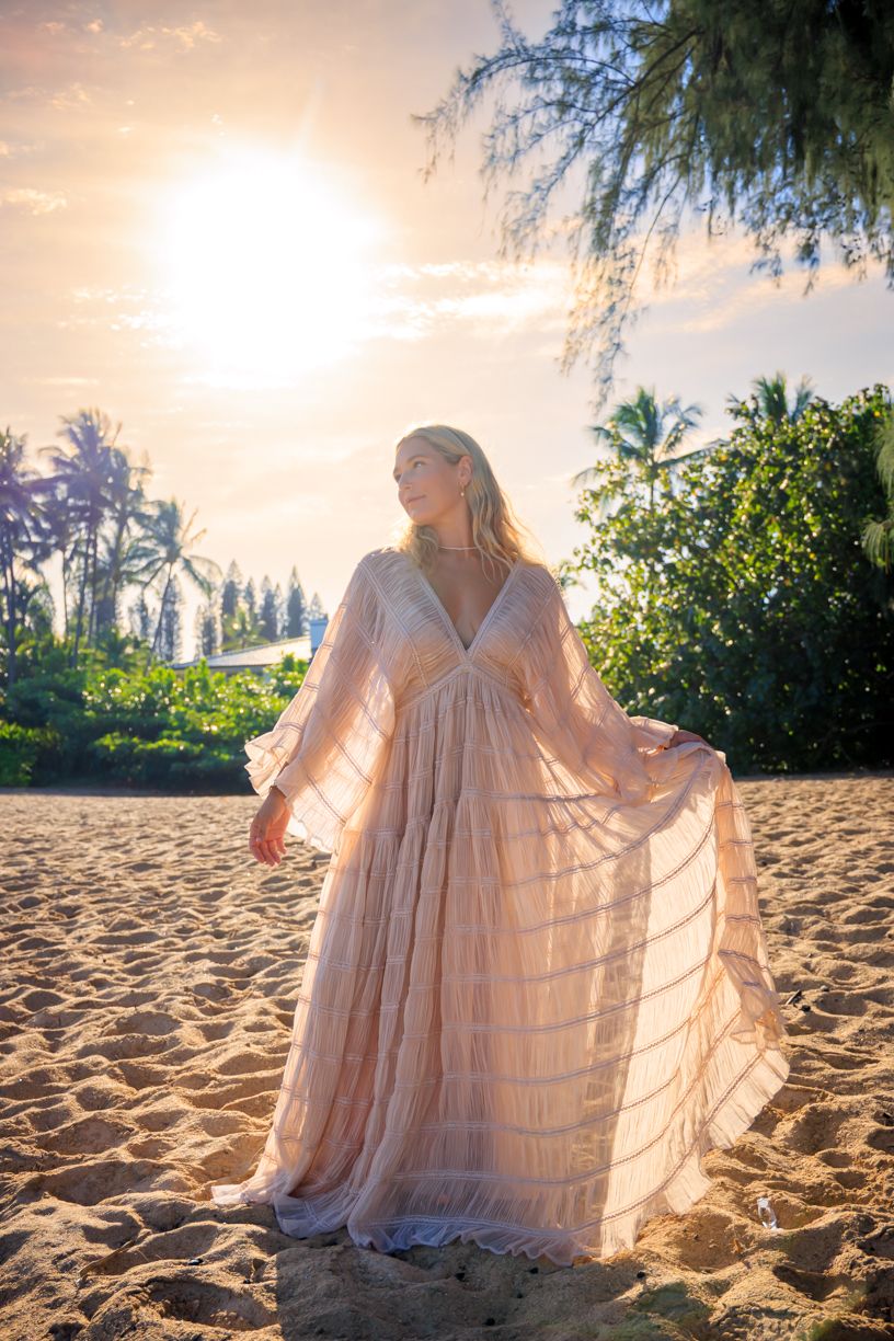 A flowing dress creates a dreamy silhouette against the sunset on a tropical beach with palm trees.