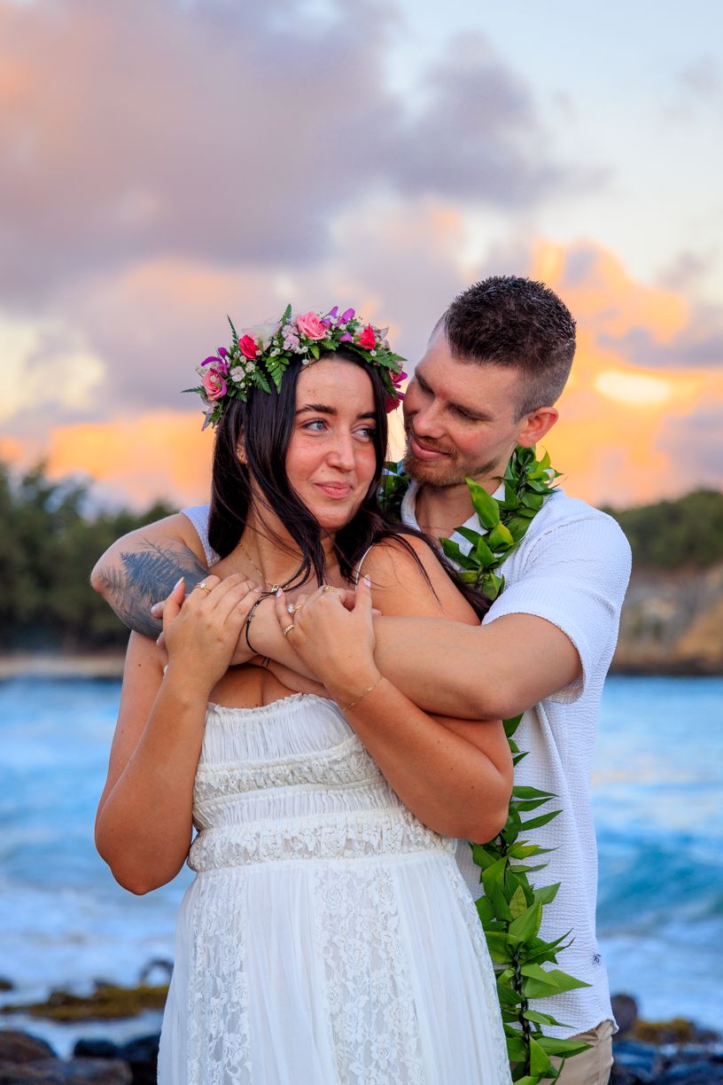 A romantic beach engagement moment at sunset with tropical flowers and ocean backdrop.