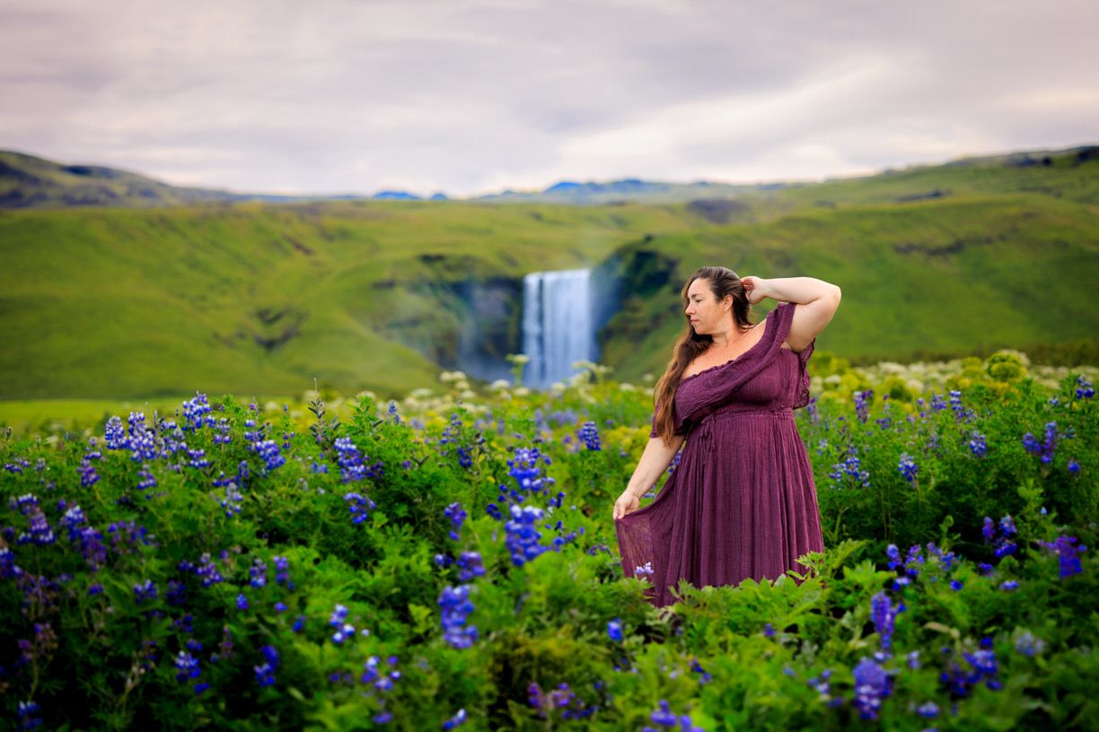 Purple wildflowers bloom in foreground of dramatic waterfall and mountain landscape.