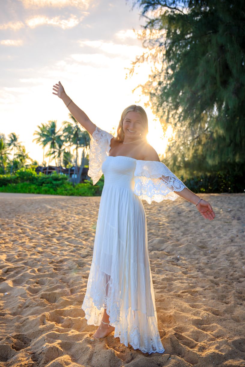 Woman in white dress twirling joyfully on tropical beach at sunset.