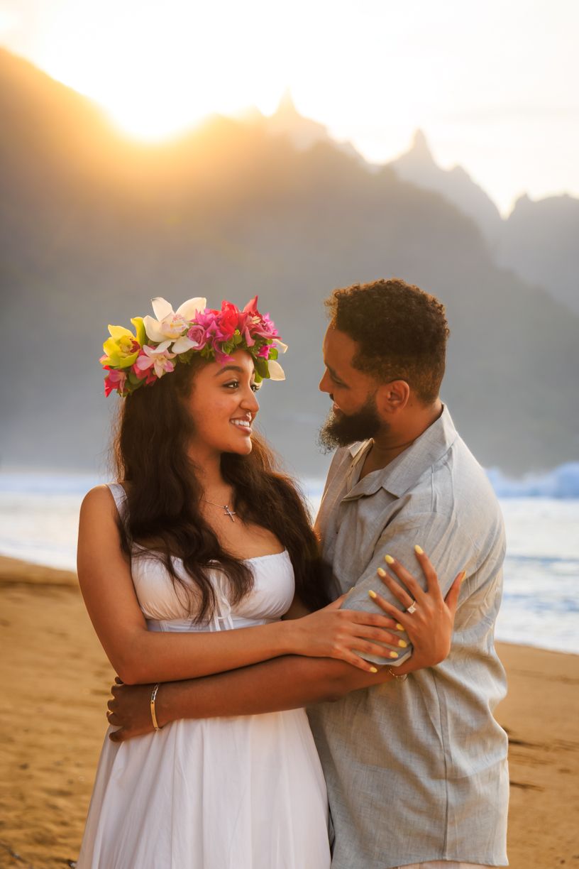 A romantic beach photoshoot at sunset with mountains creating a dramatic silhouette.
