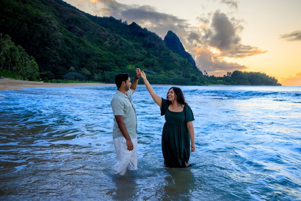 A couple plays in the ocean waves during sunset at a Hawaiian beach.