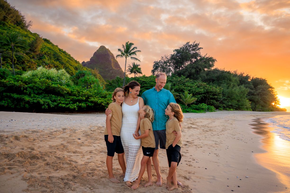 Family portrait on Hawaiian beach at sunset with dramatic mountain backdrop.