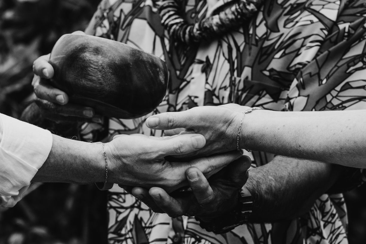 Close up of hands wearing traditional Hawaiian wedding leis in black and white.