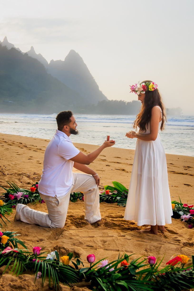 A romantic beach proposal with tropical flowers and mountains at sunset in Hawaii.