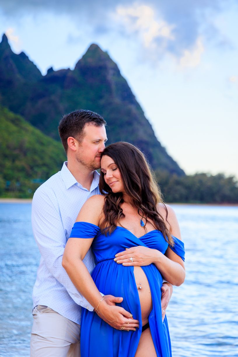 Maternity photos with dramatic mountain backdrop in Hawaii featuring couple in blue and white.