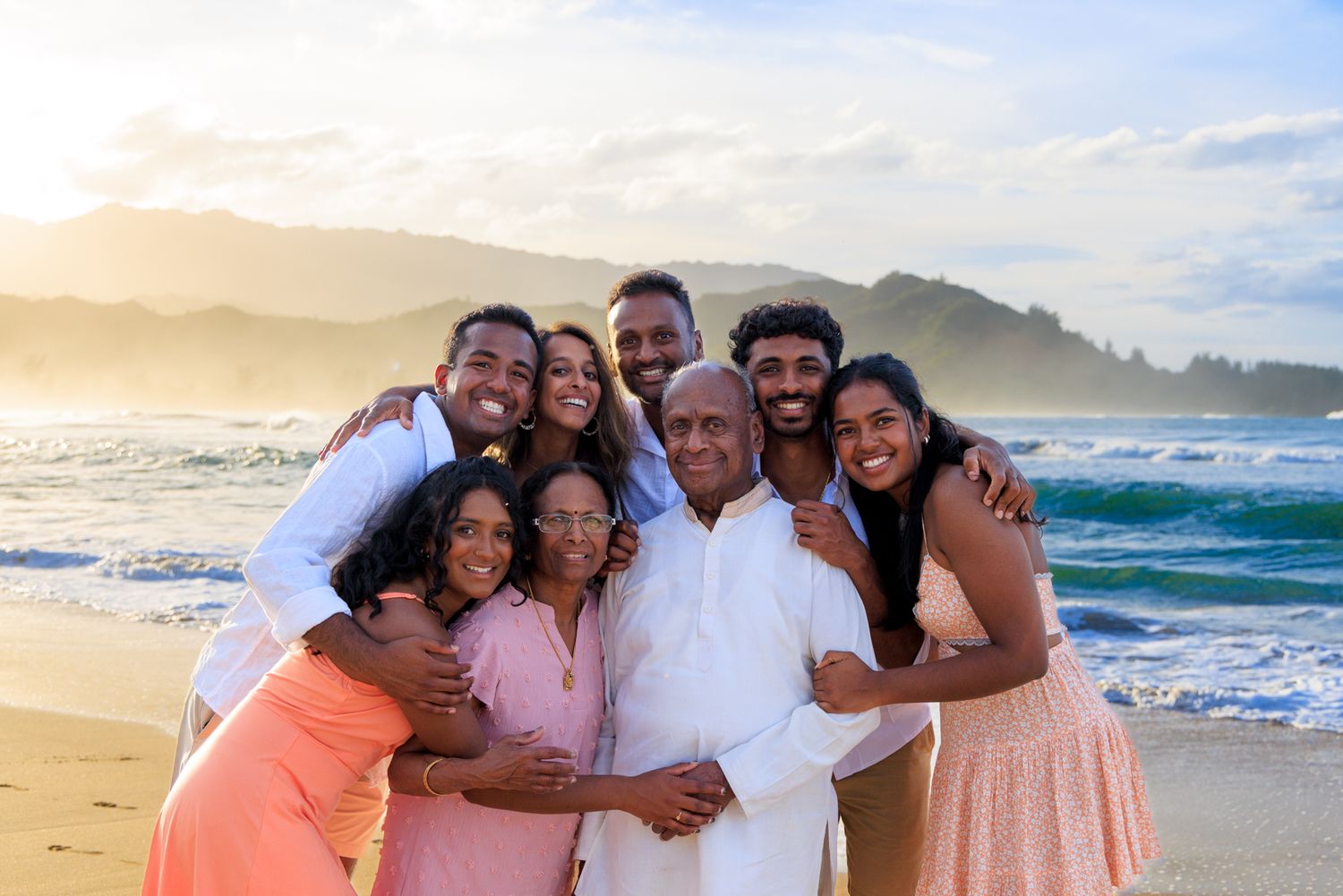 Group beach portrait with mountains and crashing waves at golden hour.