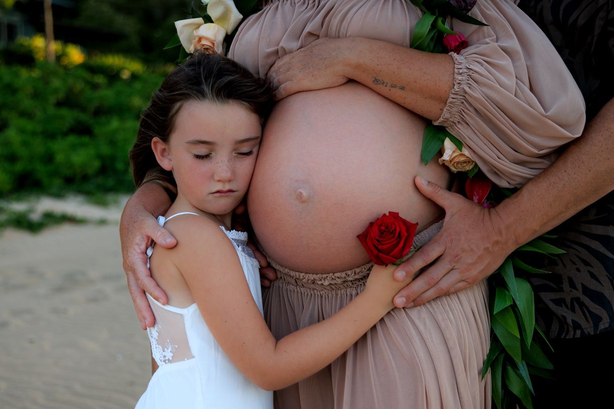 Close-up maternity photography with white dress and red rose details. Lifestyle maternity session on the shores of Hanalei Bay, Kauaʻi