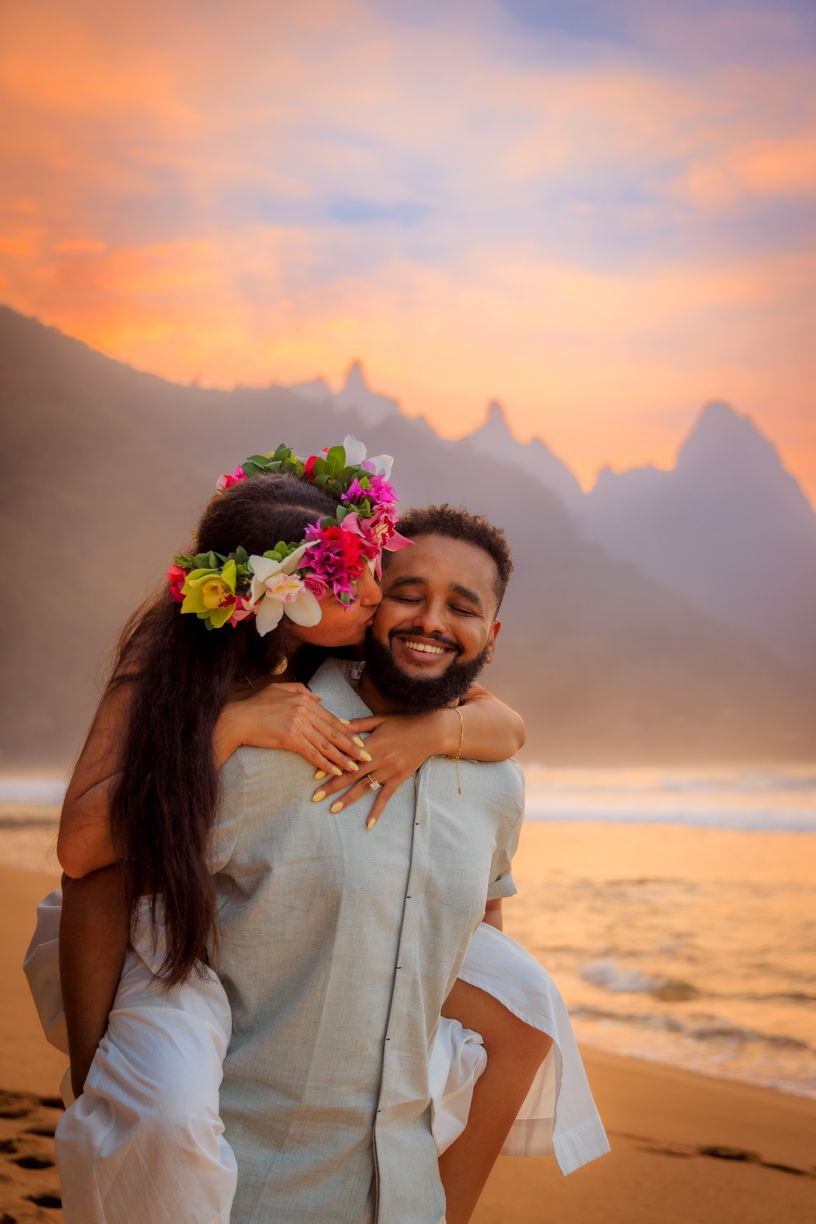 A joyful embrace on a Hawaiian beach during golden hour with mountains in the distance.