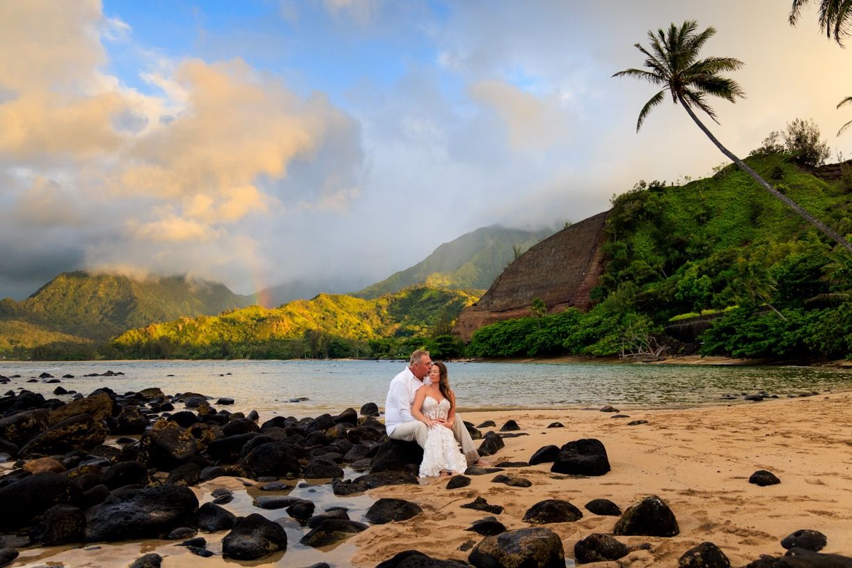 Sunset wedding photo on Hawaiian beach with volcanic rocks and palm trees.