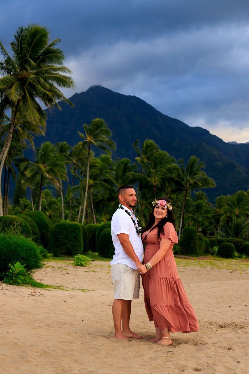 A romantic beach photoshoot with dramatic mountains and palm trees in the background.