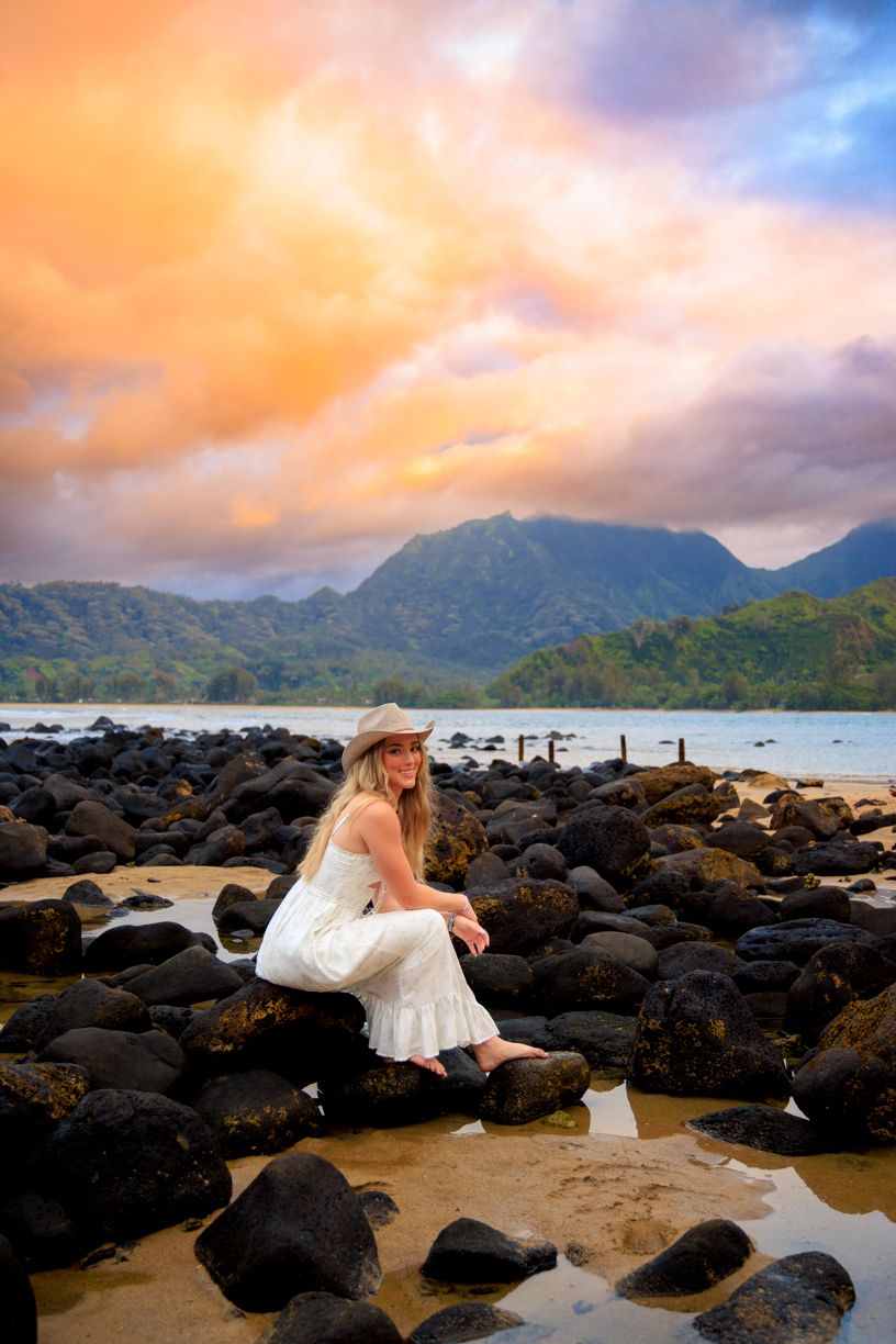 Scenic Hawaiian beach view with volcanic rocks and mountains during golden sunset.