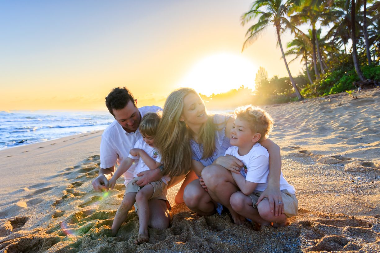 Family bonding moment captured on sandy beach during golden hour sunset.