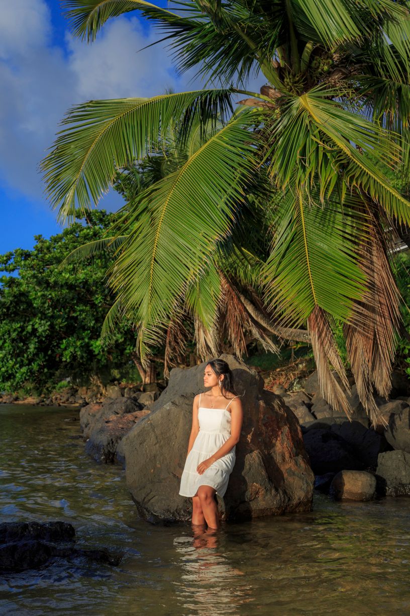 Tropical beach scene with white dress against palm trees and volcanic rocks.