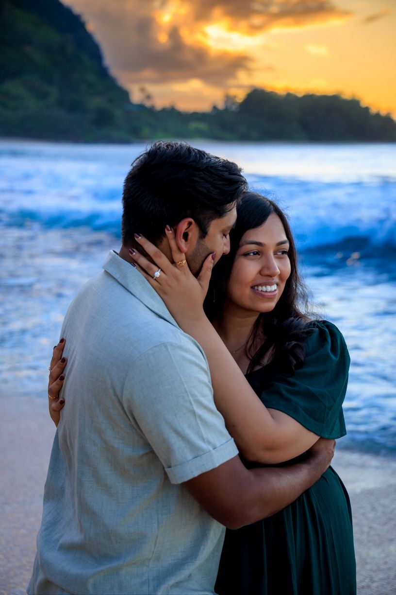 A couple shares intimate moments on a beach during golden hour with crashing waves behind them.
