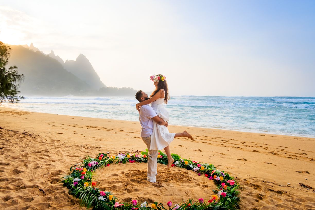 A joyful celebration inside a floral circle on a Hawaiian beach with mountain views.