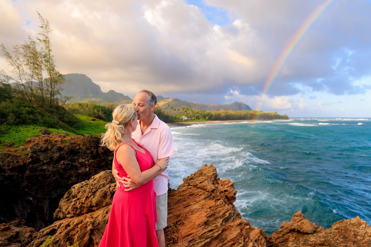 A romantic couple stands on a scenic overlook with dramatic coastal cliffs and turquoise ocean waves in Hawaii.