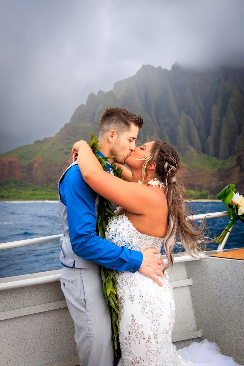 Romantic wedding photos captured on boat with dramatic Kauai coastline scenery.