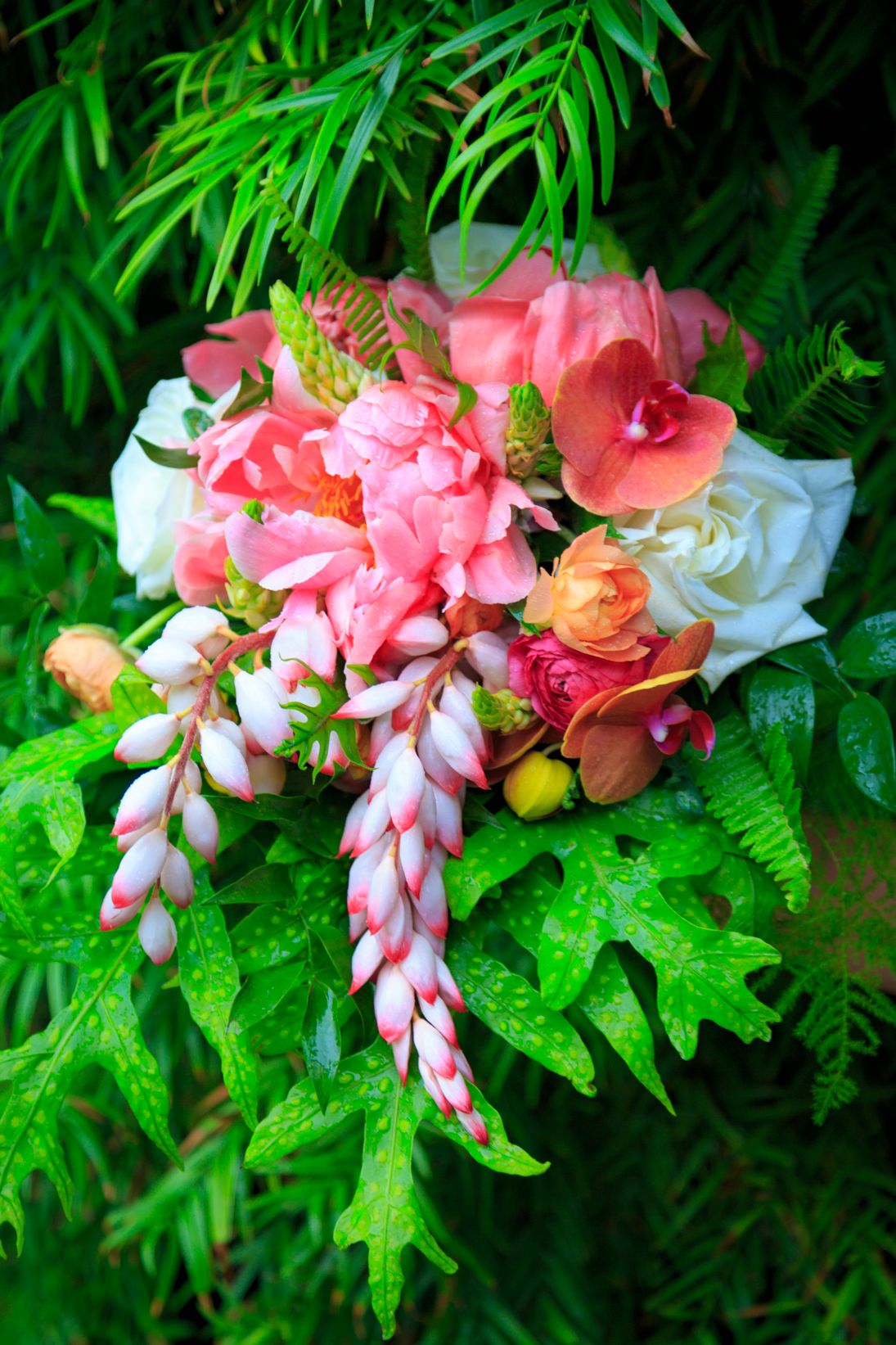 A vibrant tropical wedding bouquet with pink flowers and green foliage.