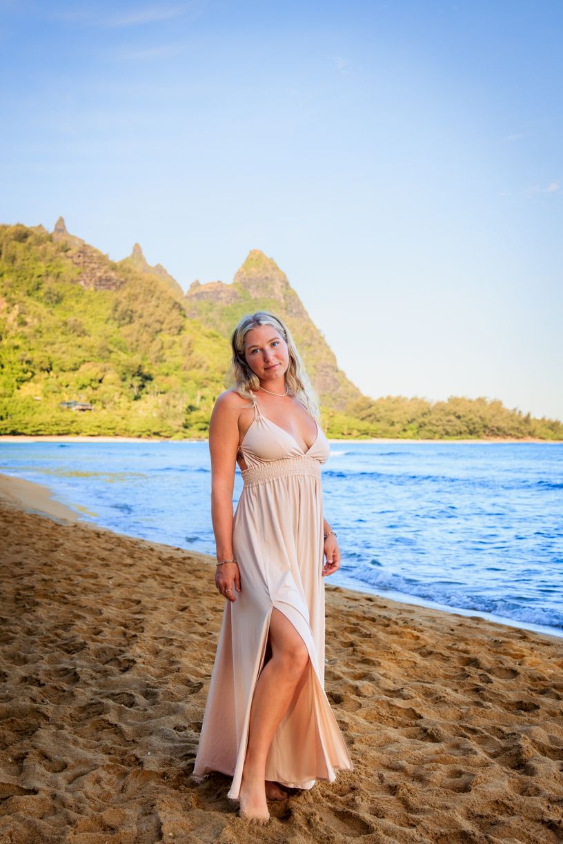 A light-colored dress flows in the ocean breeze on a beach with dramatic mountain peaks in the distance.
