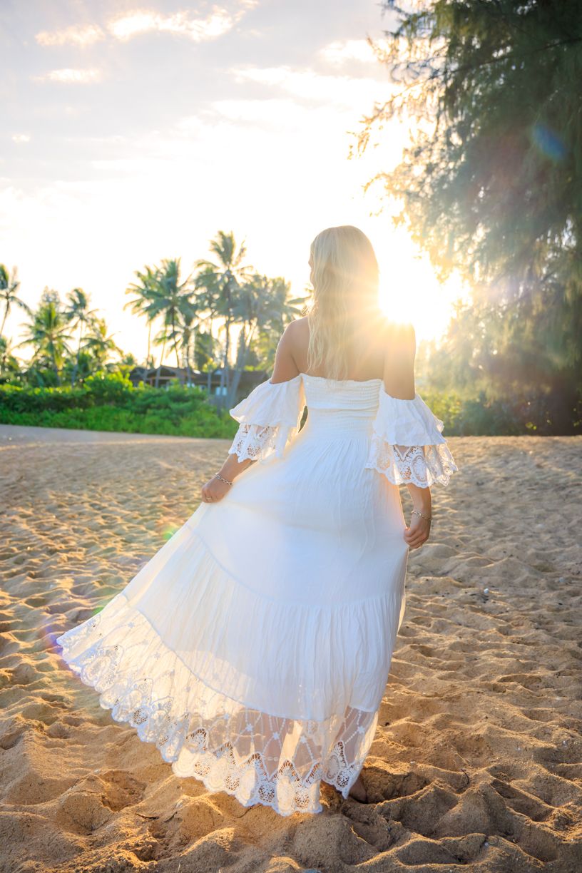 White lace dress twirling on sandy beach with palm trees and golden sunlight.