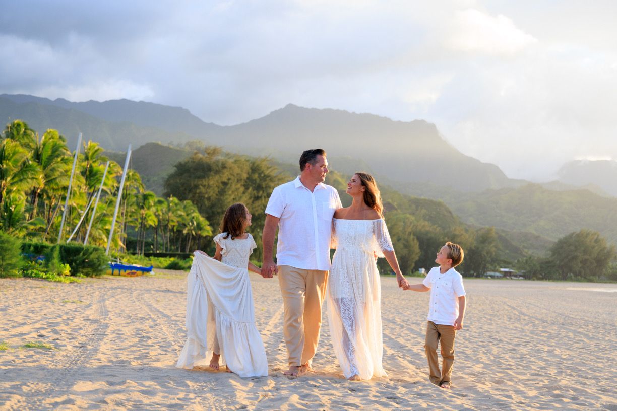 A family of four walking together on a sandy beach with mountains in the background.