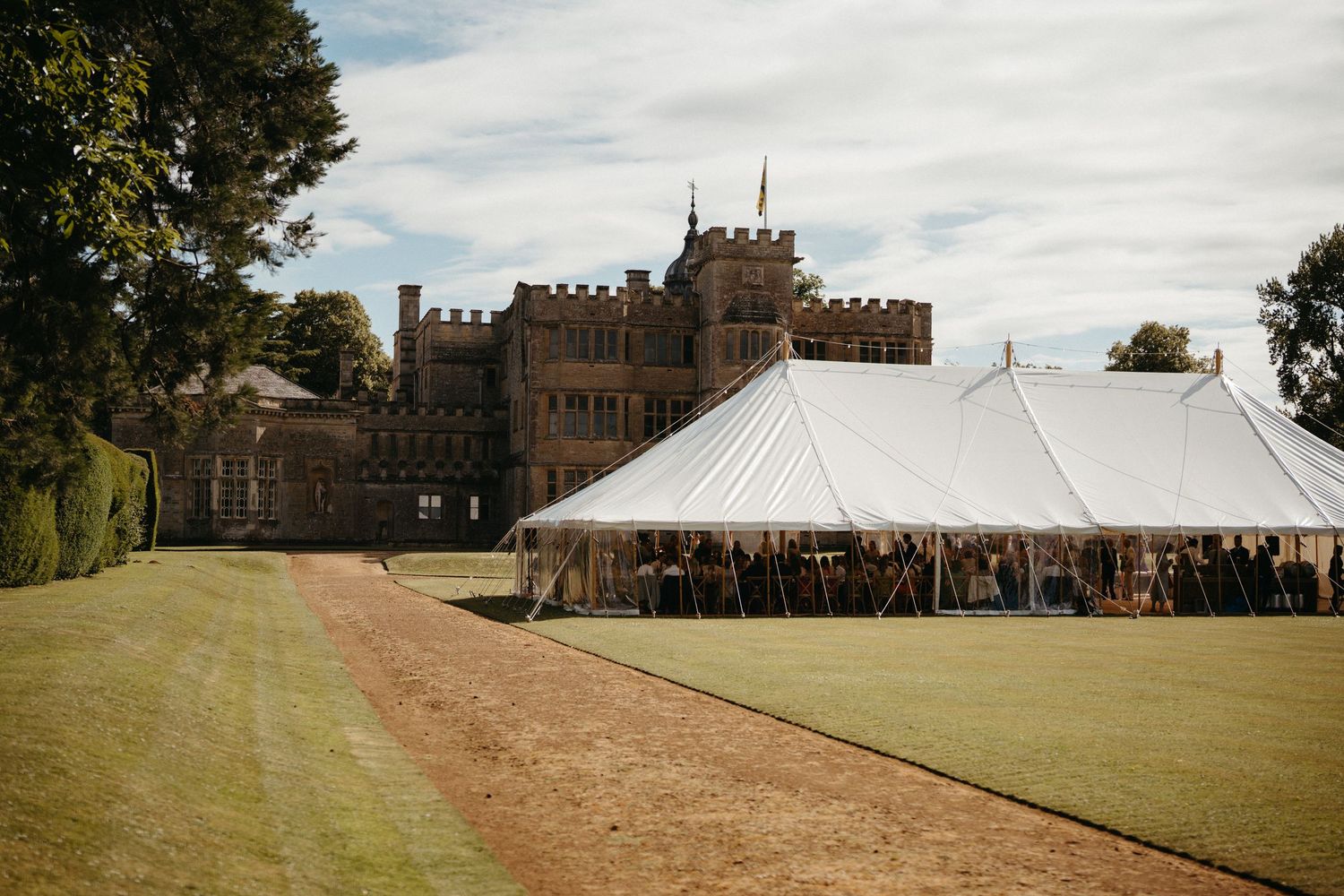 Large white wedding tent set up on expansive lawn with historic manor house in background.