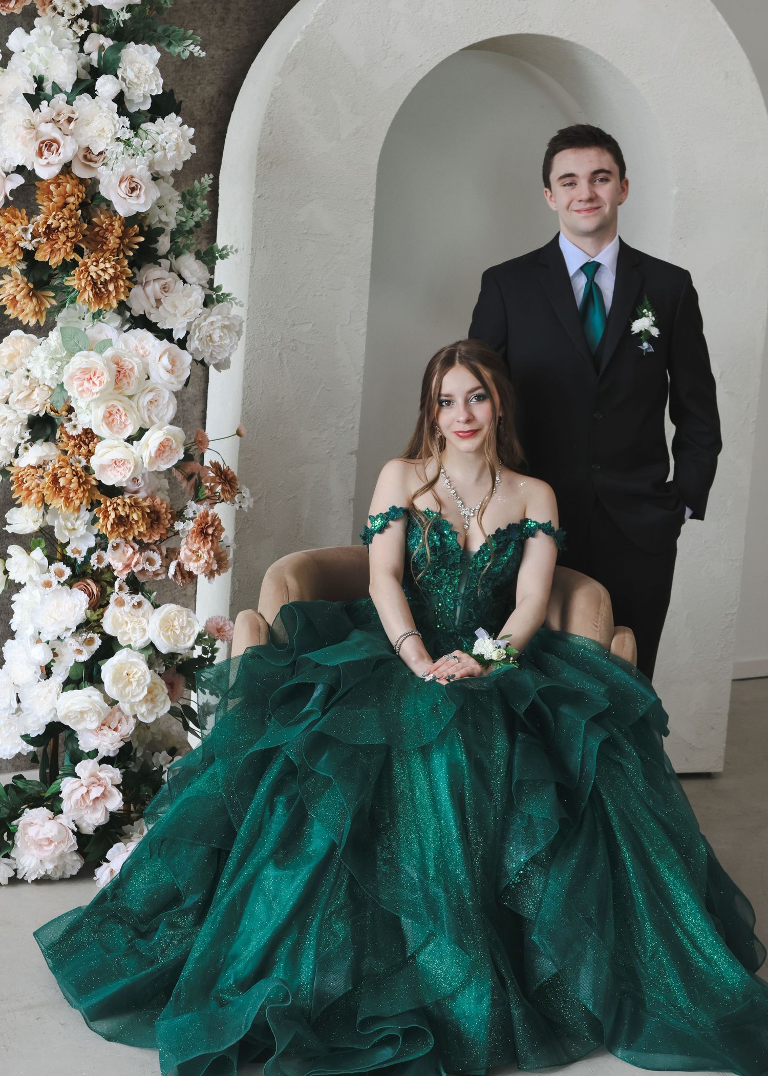 Couple posing with woman in emerald green ball gown seated and man in black suit standing.