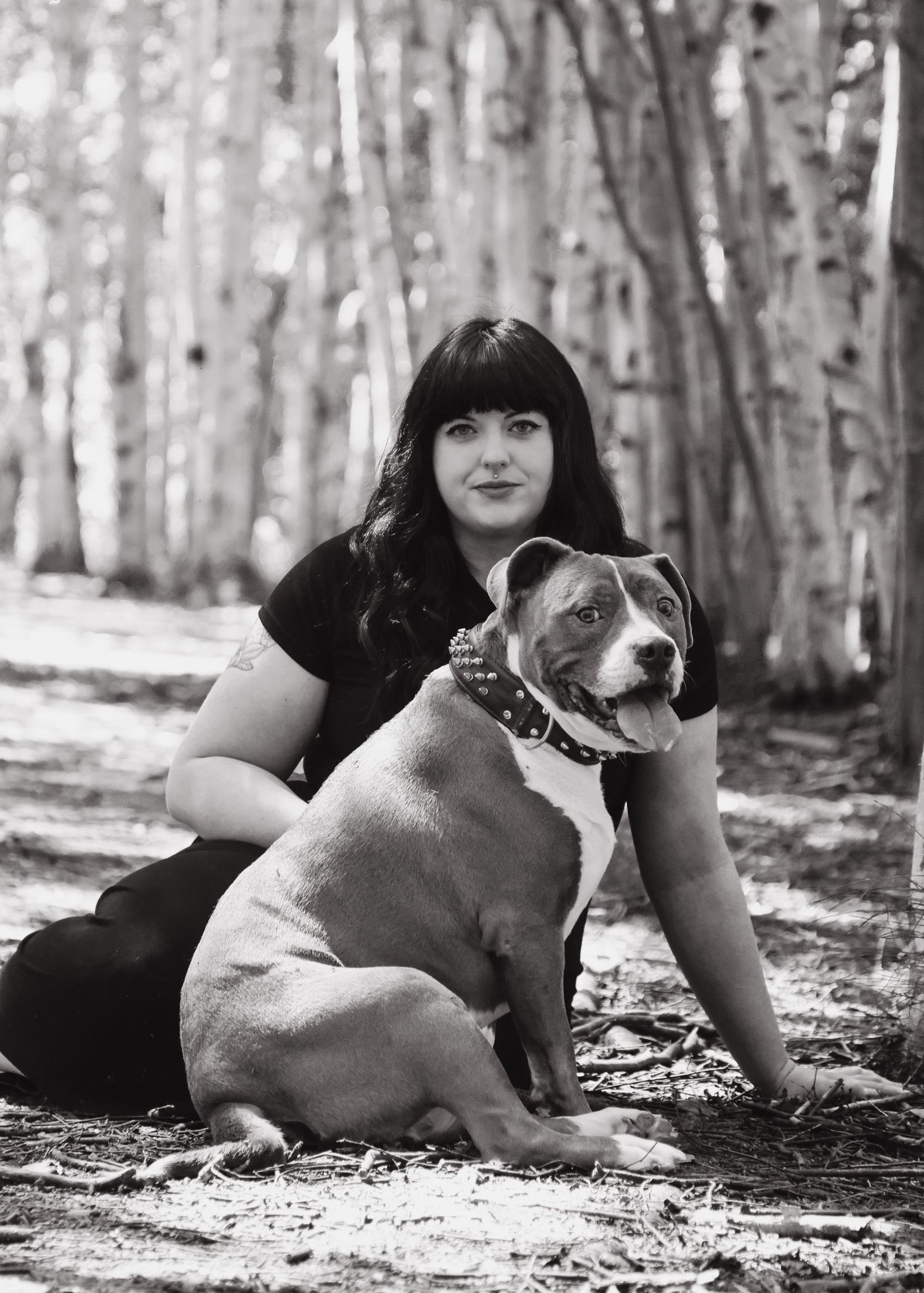 Black and white portrait of woman with pit bull dog in forest setting.