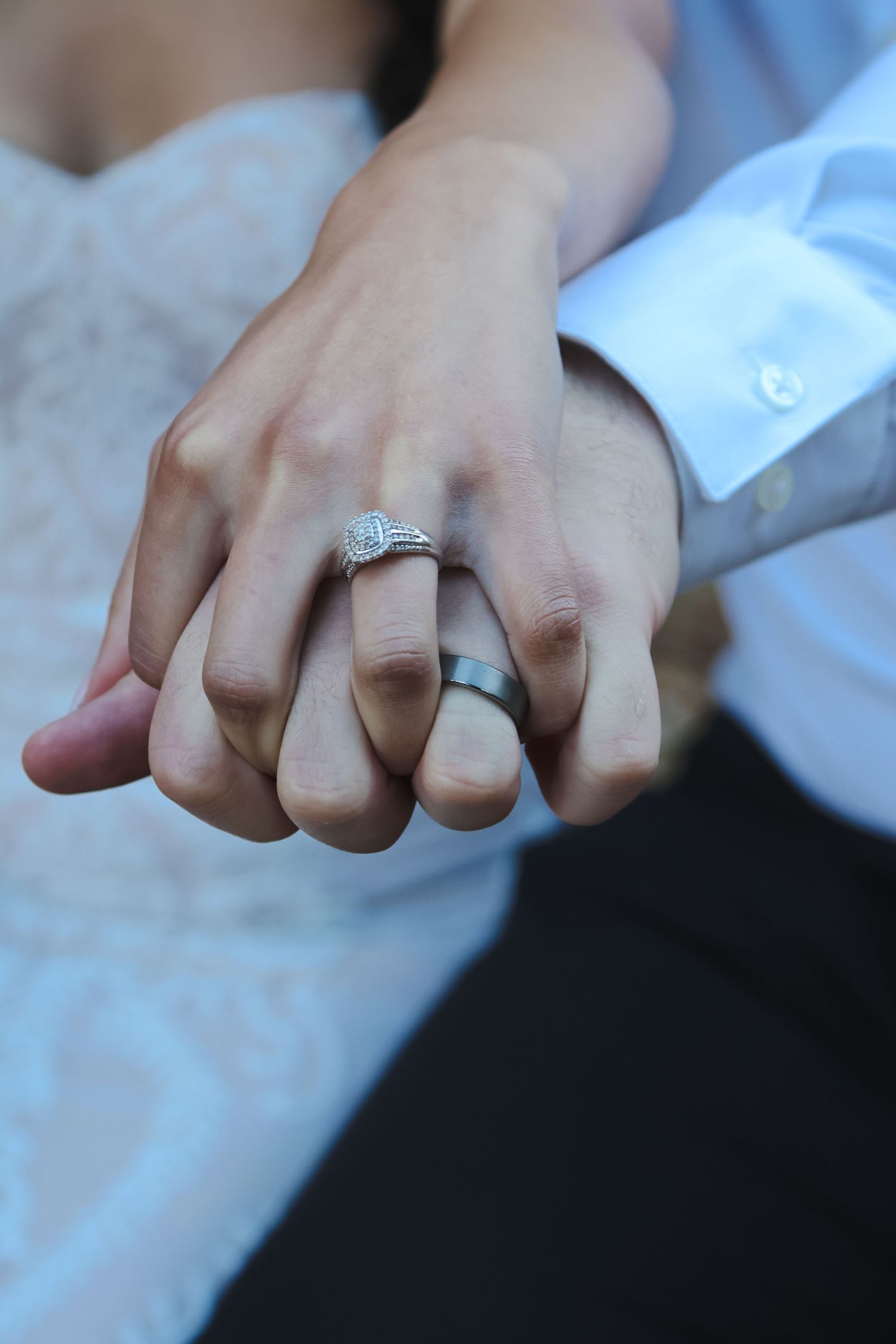 Close-up of bride and groom hands showing diamond engagement ring and wedding band.