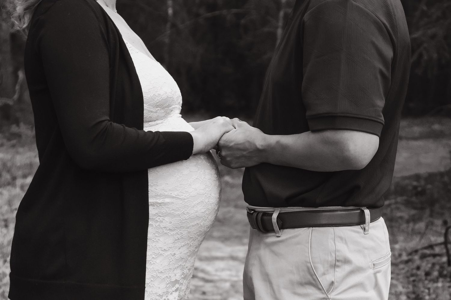 Black and white photo of a pregnant woman holding hands with her partner outdoors.