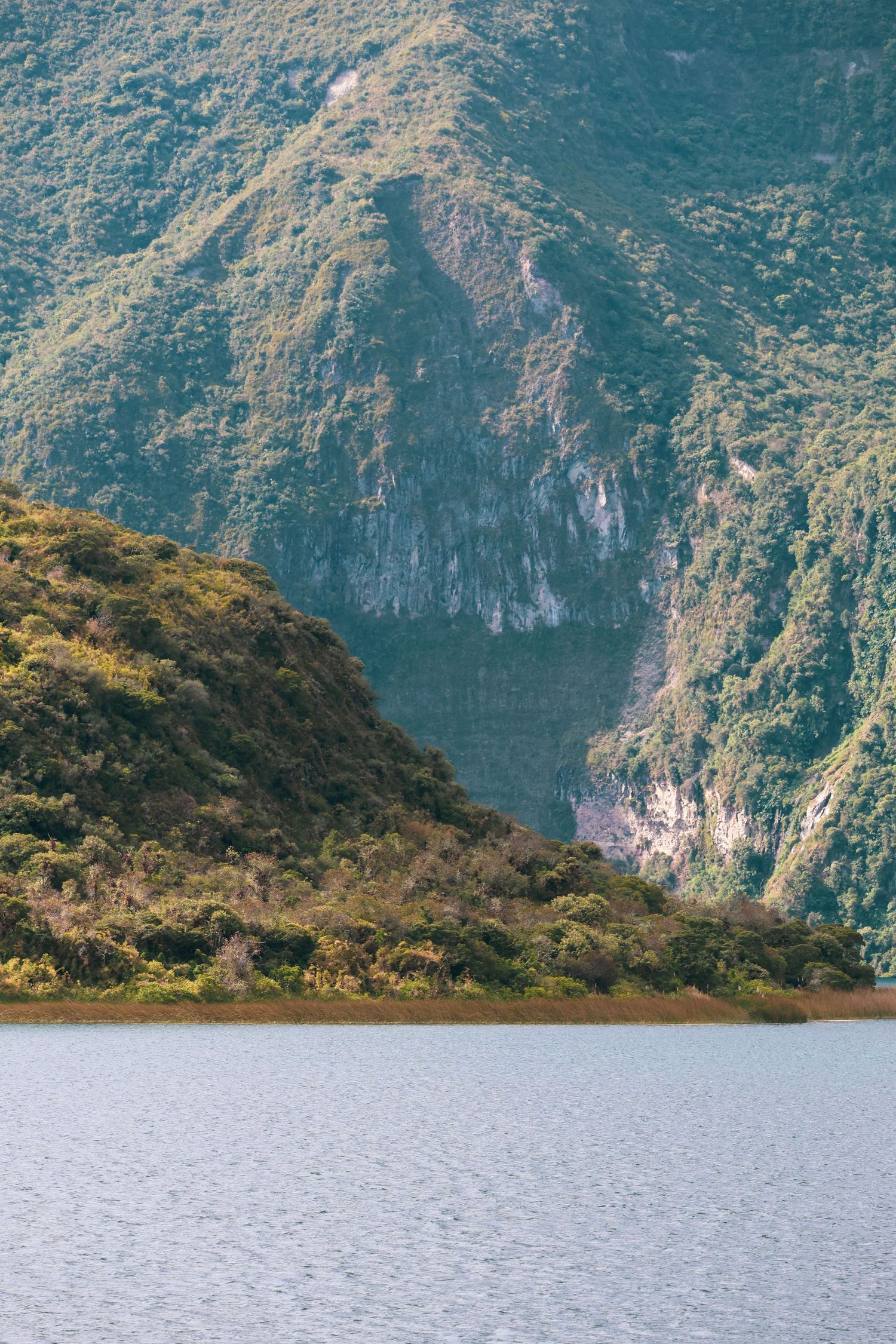 Serene mountain lake surrounded by lush green steep cliffs and dense vegetation in a dramatic natural landscape.