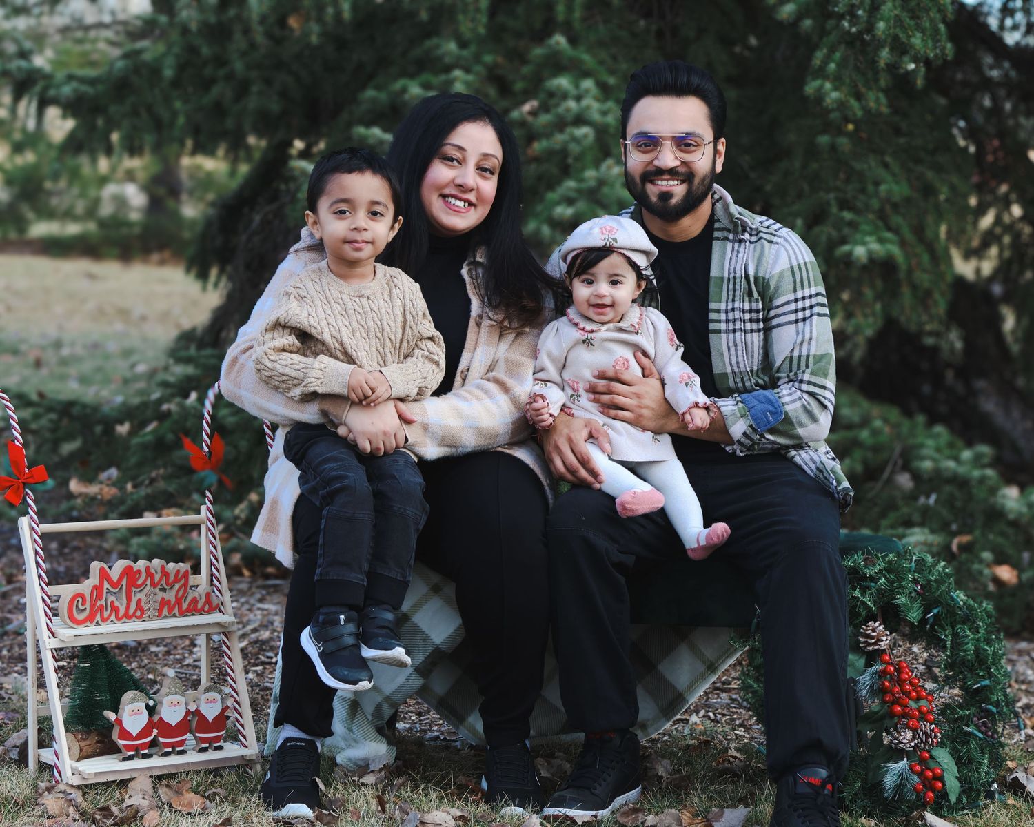 Joyful family of four poses outdoors near Christmas decorations with two young children.