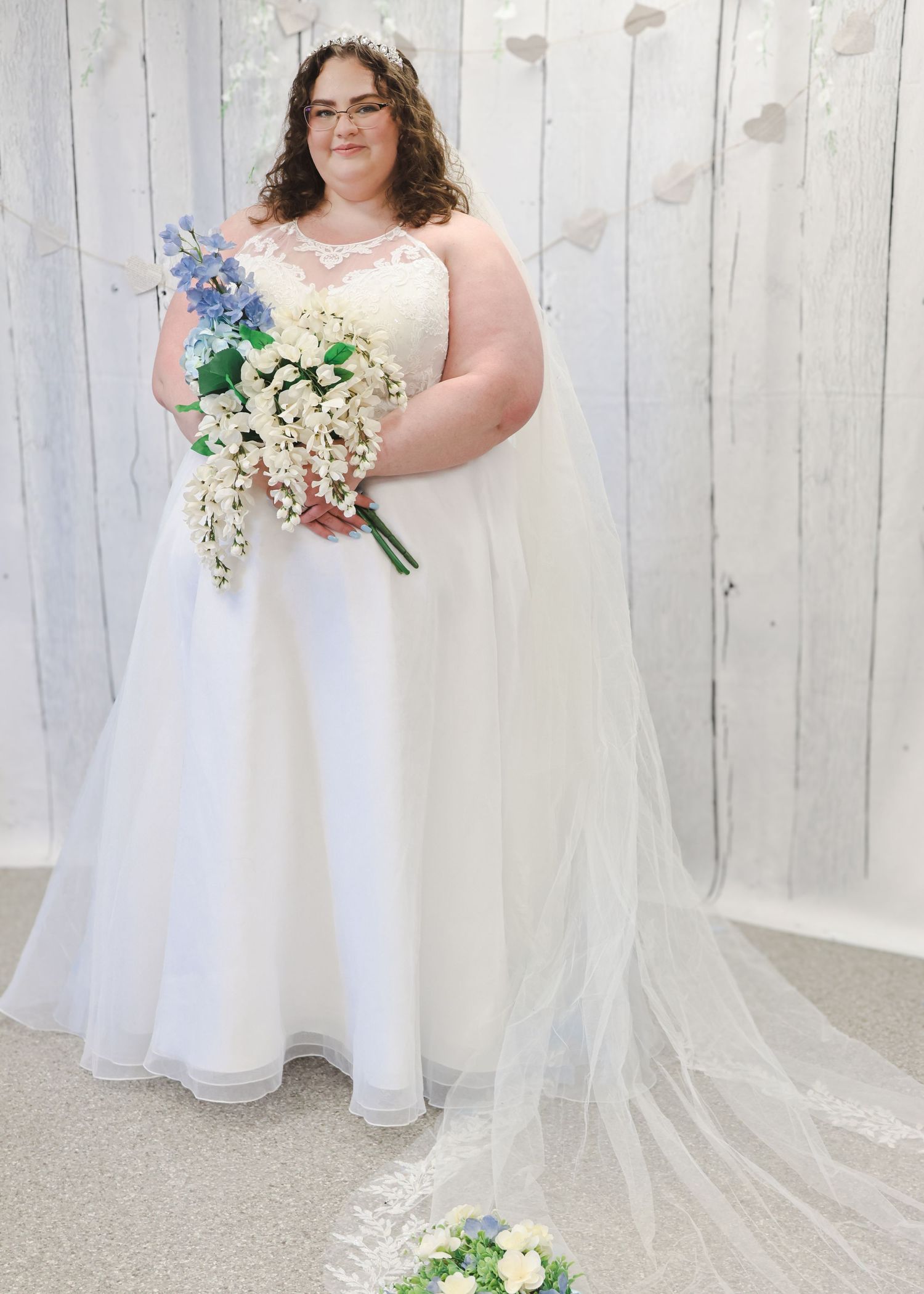 Bride in a white lace ball gown with veil holding a blue and white cascading bouquet.