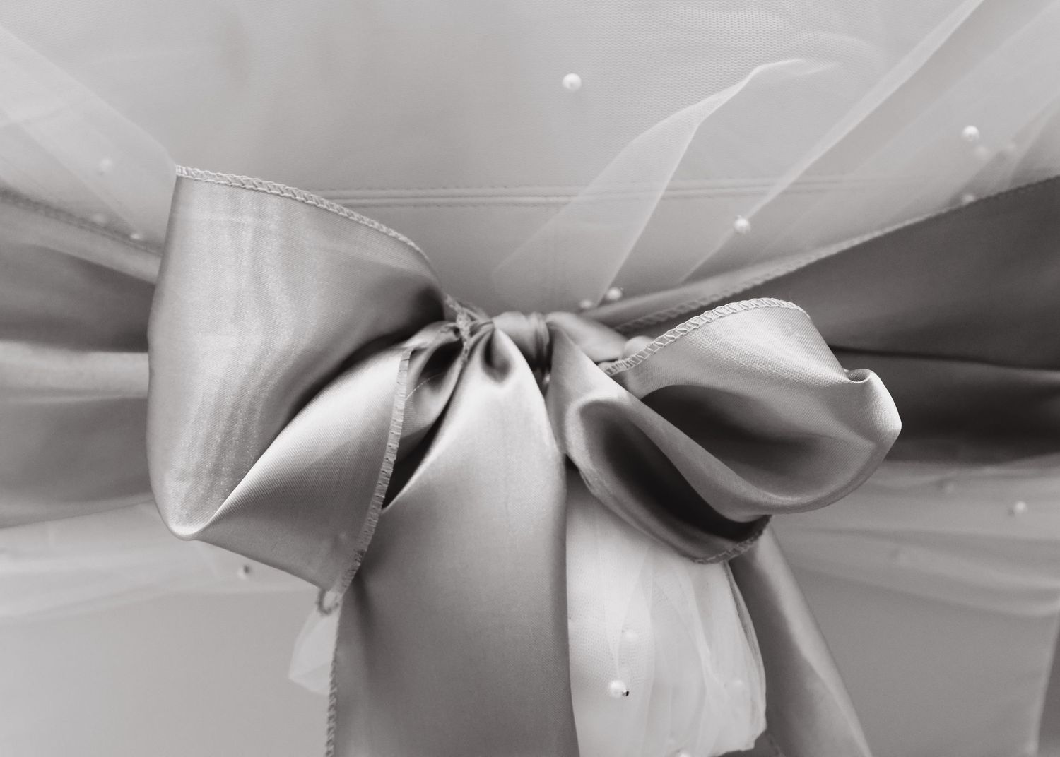 Elegant gray satin bow on a white tulle wedding chair cover with pearl accents.