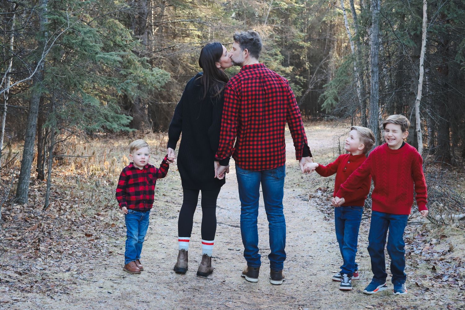Family of five walks hand-in-hand down autumn forest trail in coordinating red and black outfits.