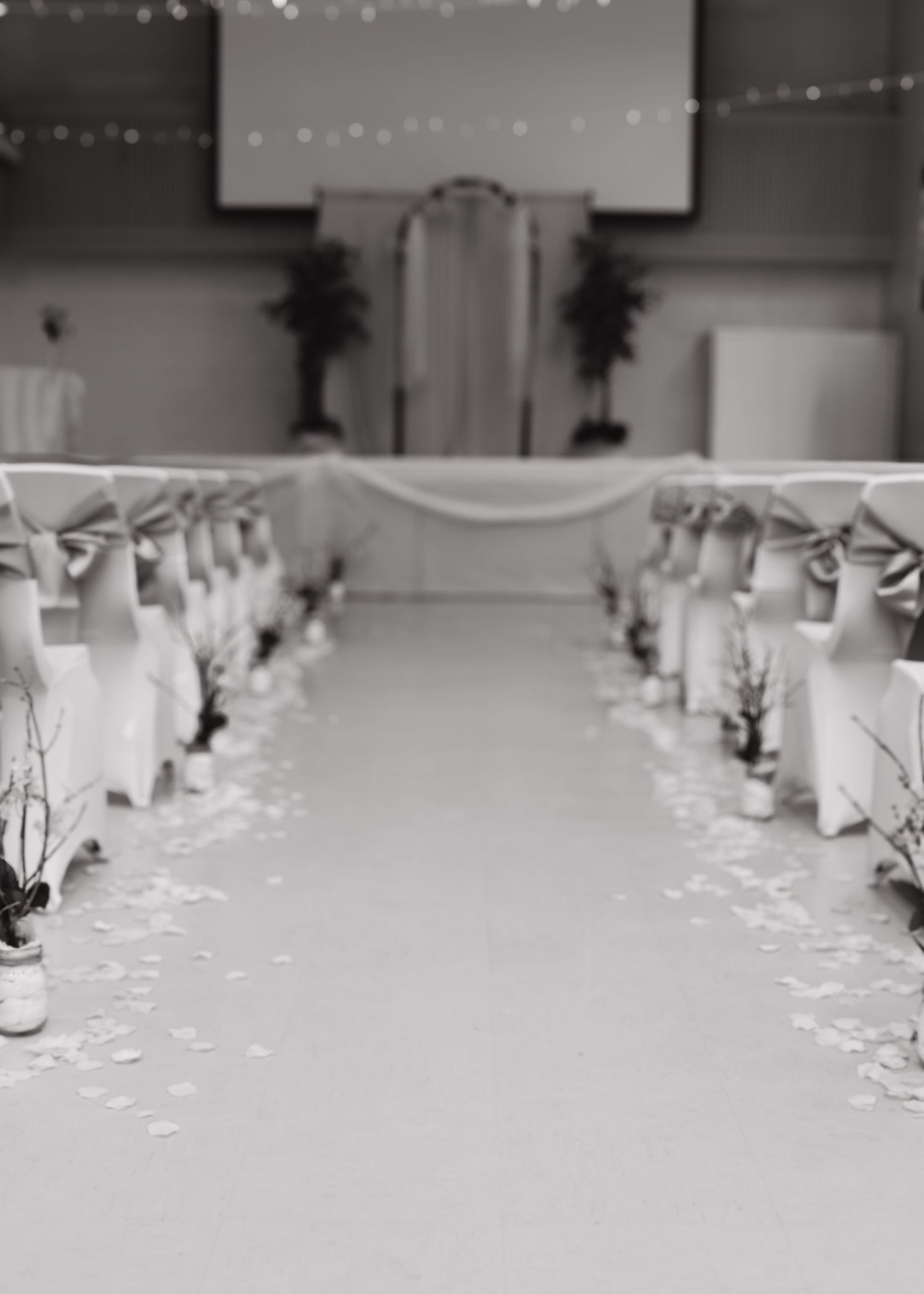 Black and white photo of a wedding ceremony aisle with white chair covers and floral decor.
