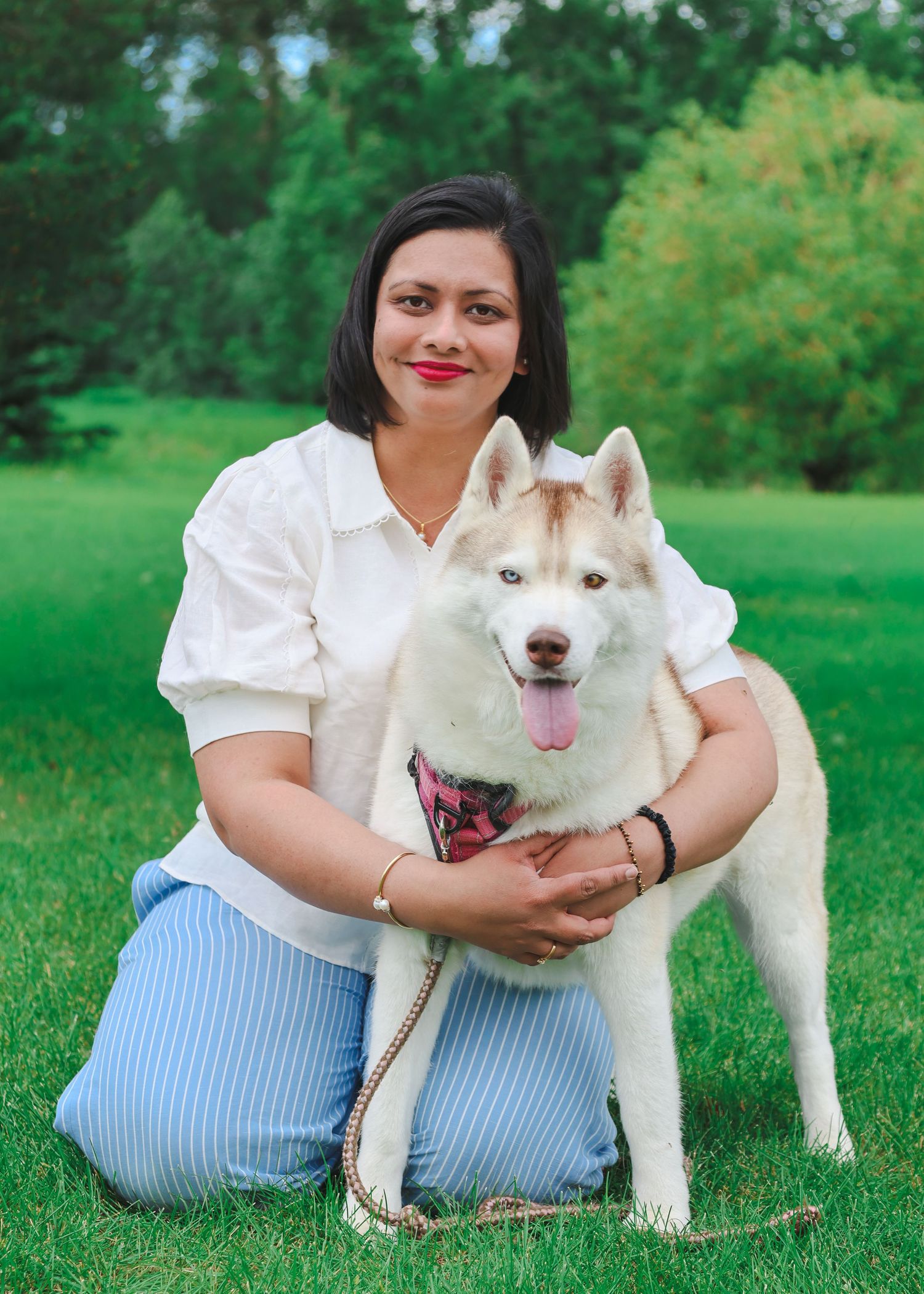 Woman in white blouse hugging a white Siberian Husky dog on green grass in a park.