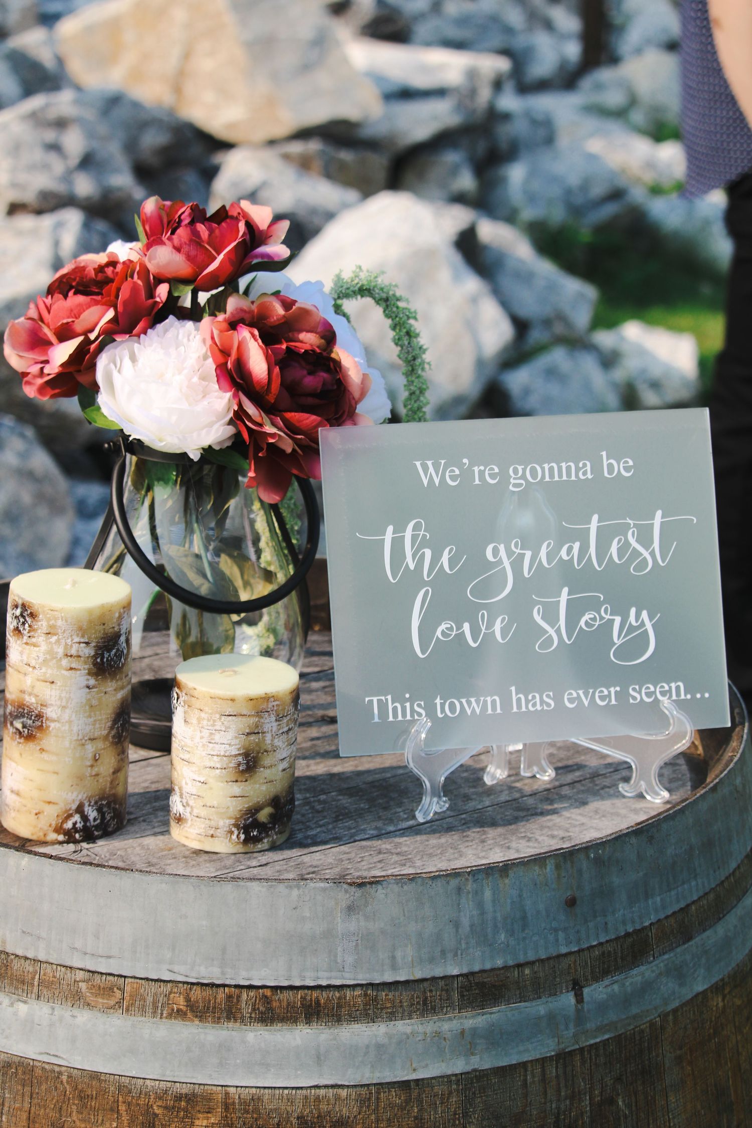 Rustic wedding decor with a romantic sign, red and pink flowers, and birch candles on a wooden barrel.
